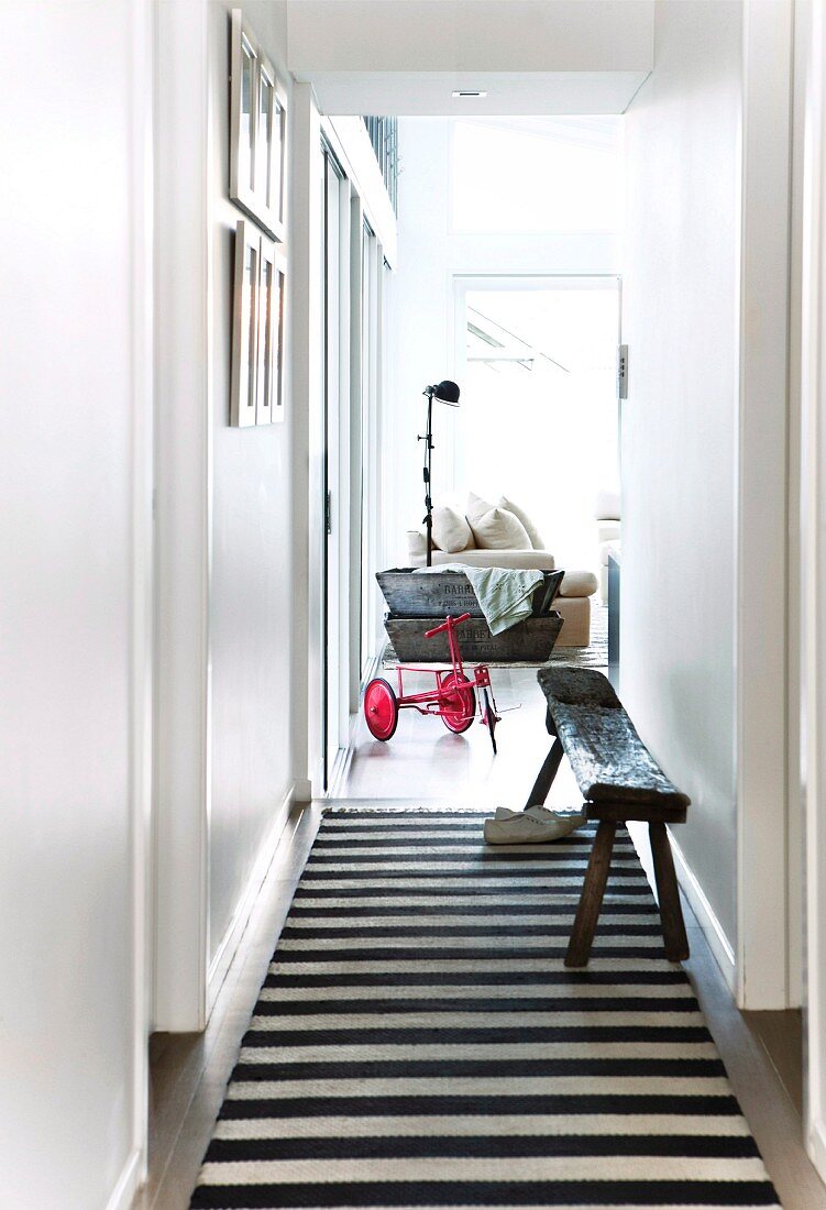Narrow hallway with black and white striped runner and view through open door of vintage tricycle in modern living room