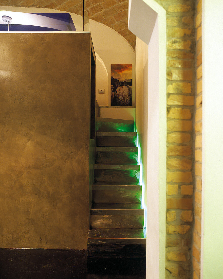 Schmale Galerietreppe mit indirekter Beleuchtung neben eingestelltem Raumkubus unter historischem Ziegelgewölbe