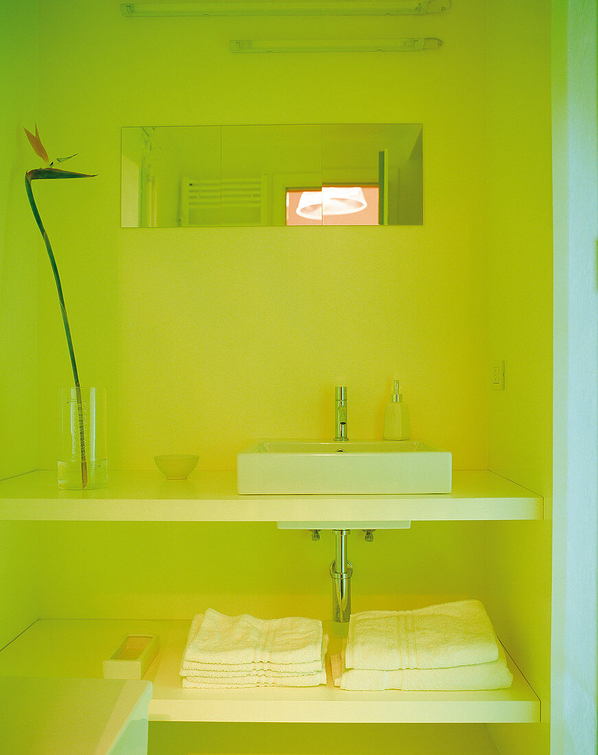 In gelbes Licht getauchte Badnische mit eckigem Aufsatzbecken auf offenem Waschtisch mit Handtuchablage