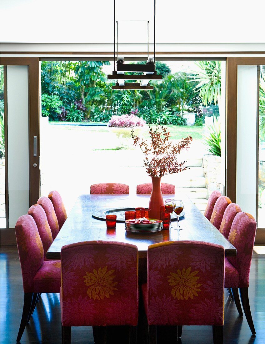 Gepolsterte Stühle mit gemustertem Bezug am Esstisch vor offener Terrassentür mit Gartenblick