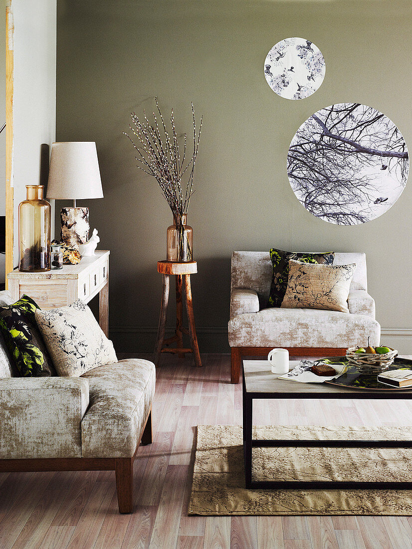 Armchairs, coffee table, console table and round prints on taupe walls of living room