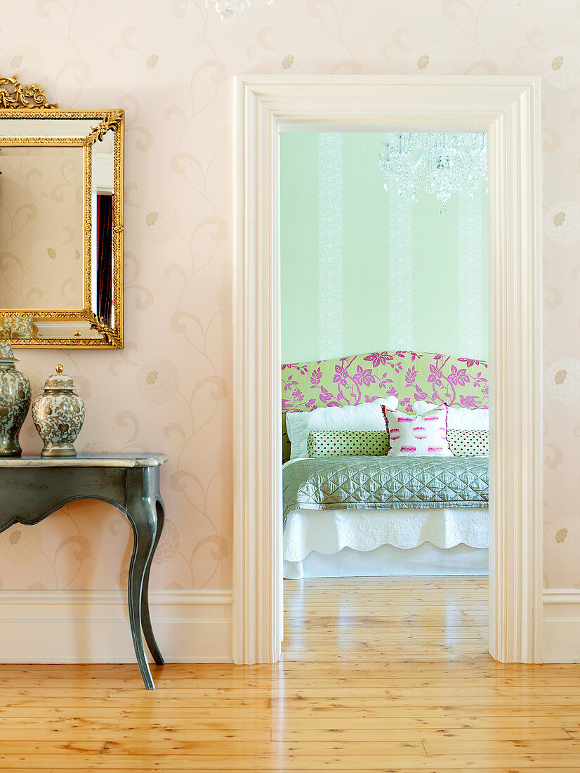 Blick ins Schlafzimmer mit prunkvollem Doppelbett und darüberhängendem Kristallleuchter; im Flur ein Wandtisch mit goldgerahmtem Spiegel