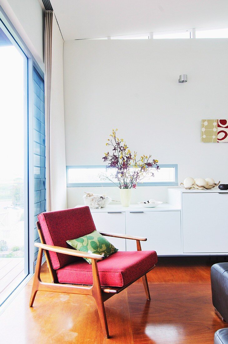 Sessel im 50er Jahre Stil vor weißem Sideboard und Fensterfront in Wohnzimmerecke