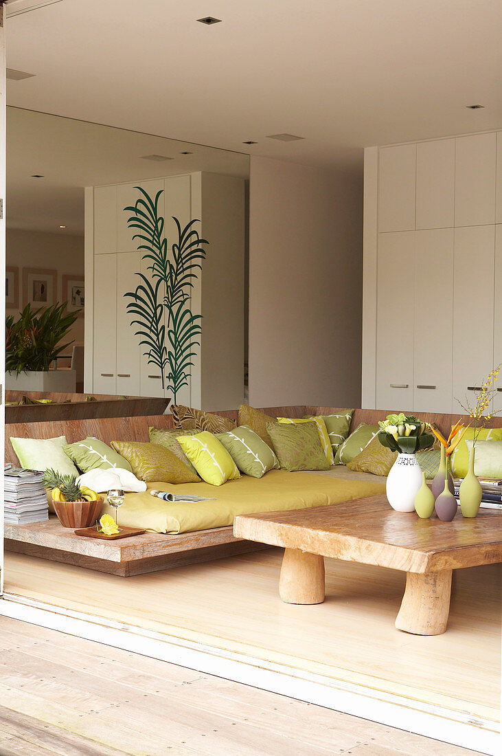 Loungeecke mit Polstern auf bodennahem Holzgestell und rustikalem Couchtisch in modernem Wohnzimmer
