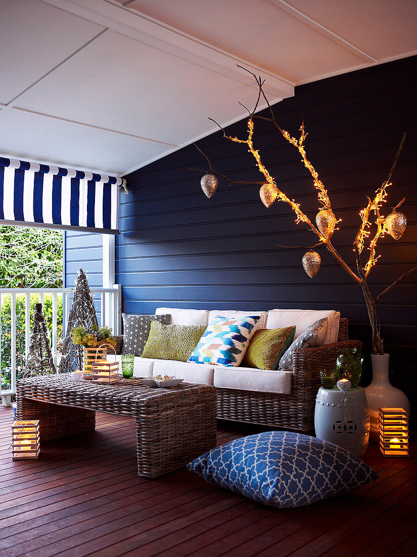 Couchtisch und Sofa aus Rattangeflecht vor blau getönter Holzwand auf der Veranda