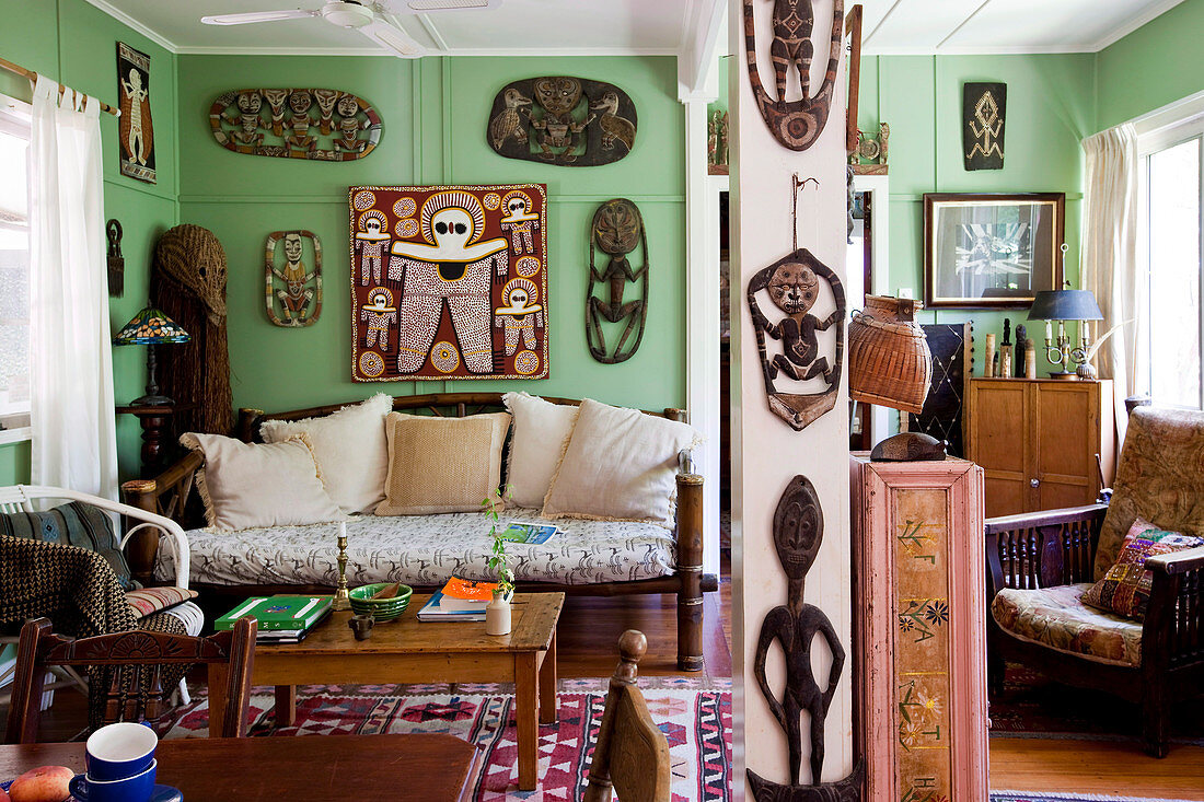 Gemütliches Wohnzimmer mit antiker Möbeleinrichtung und afrikanischen Holzschnitten an grün getönter Wand