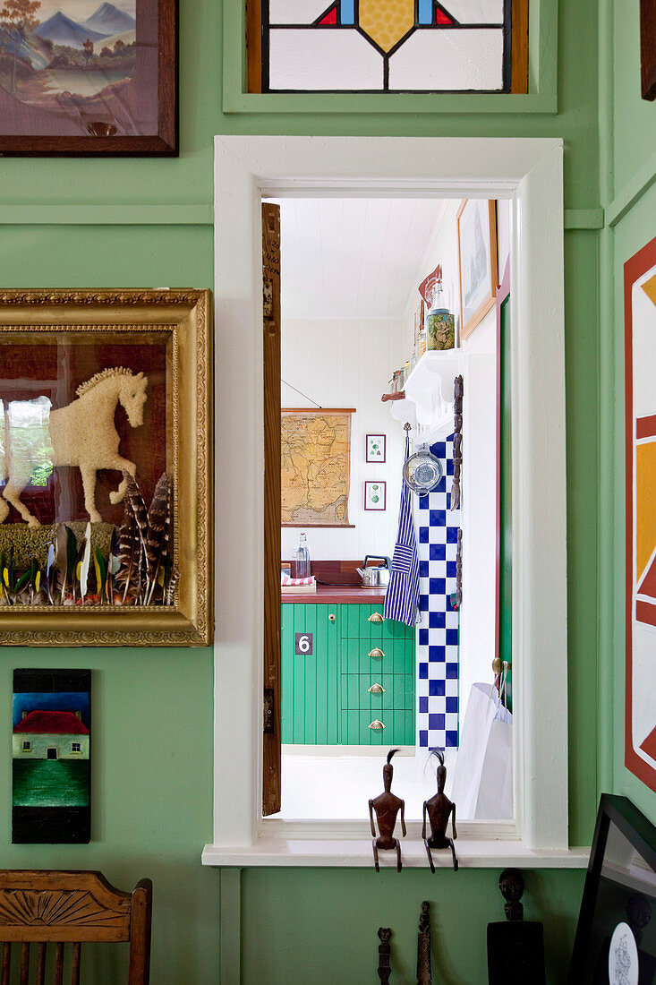 Gerahmte Bilder an grüner Zimmerwand mit Fenster und Blick auf Küchenzeile