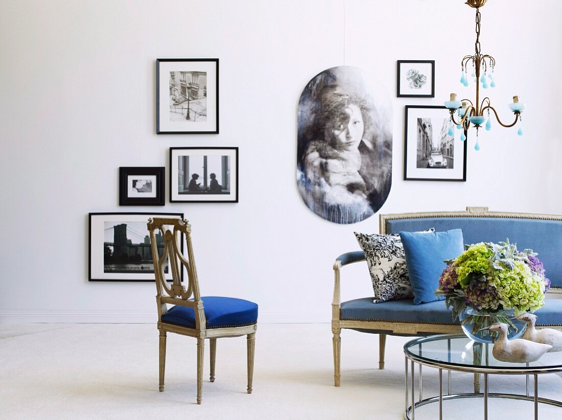 Antike Sofagarnitur mit blauen Polstern und moderner Couchtisch mit Glasplatte vor Wand mit gerahmten Photographien
