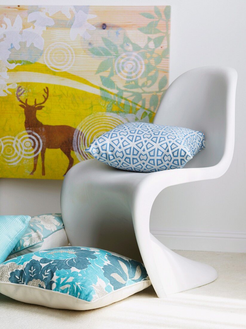Kissen auf Boden und auf Klassiker Stuhl aus weißem Kunststoff vor Bild an Wand