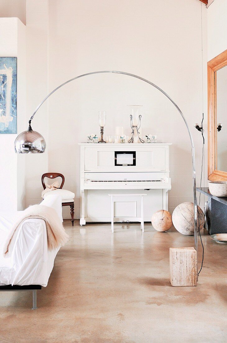 Bogenlampe im Bauhausstil vor weißem, antikem Klavier in Wohnzimmerecke