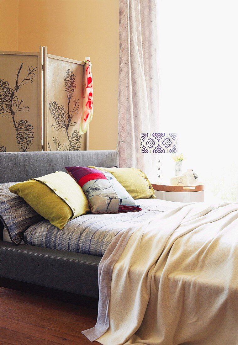 Screen with a floral pattern; in front a French bed with colorful decorative pillows