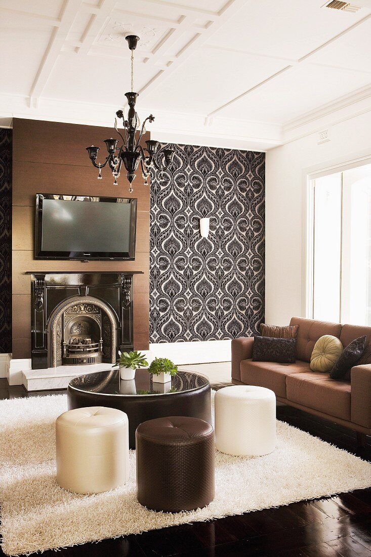 Elegant interior with open fireplace, leather-covered pouffes on white flokati-style rug and couch in various shades of brown