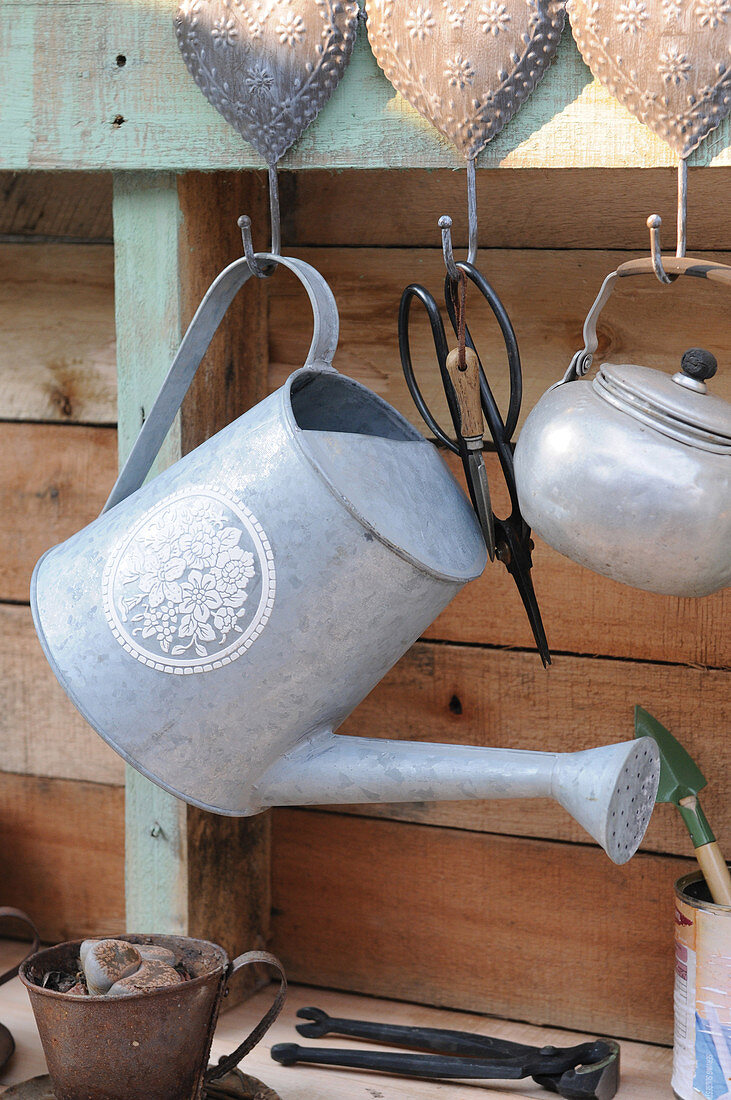 Metal watering can hanging against wooden wall