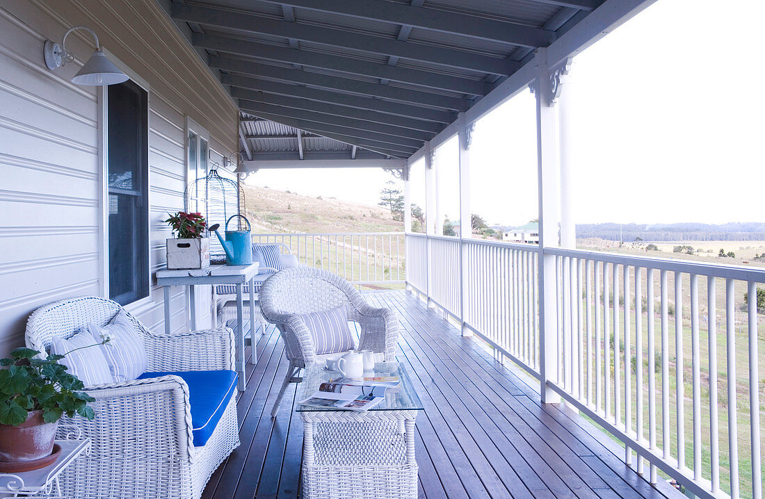 Terrassenmöbel aus weißem Geflecht auf Veranda eines ländlichen Holzhauses