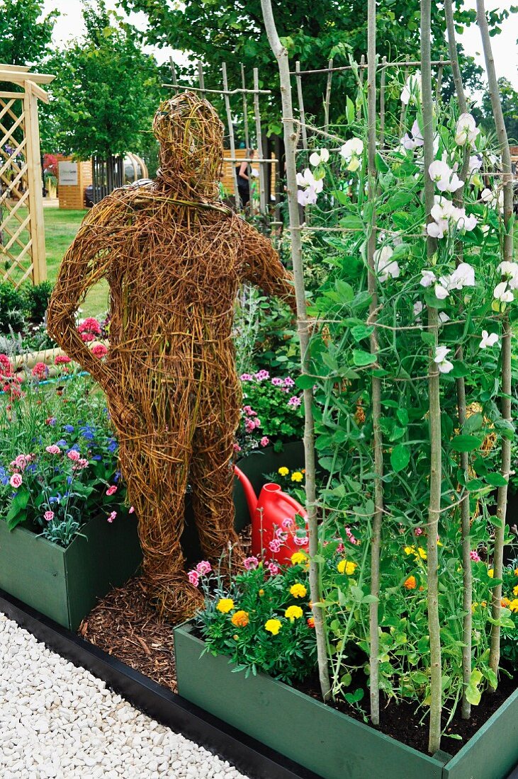 Life-sized straw figure of a human between flowerbeds