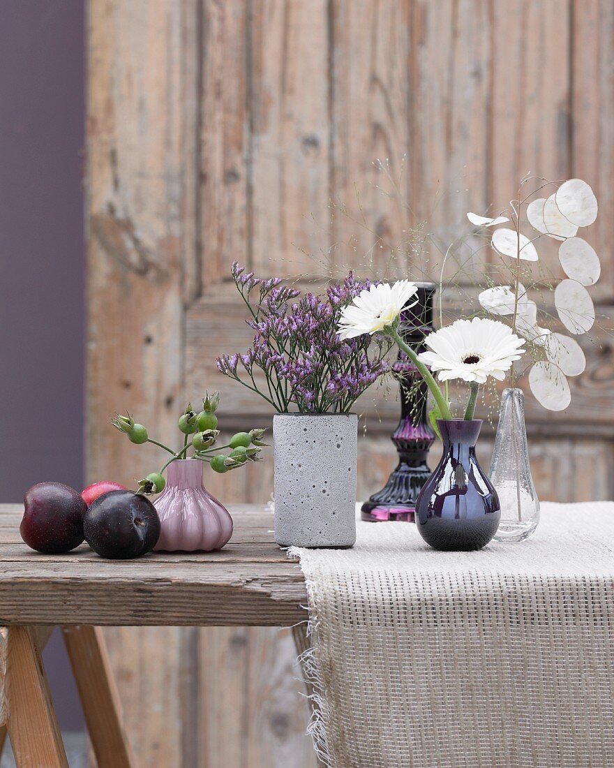 Blumenvasen und Pflaumen auf Holztisch