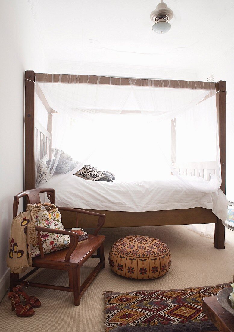 Wooden canopy bed in ethnic bedroom with wooden armchair