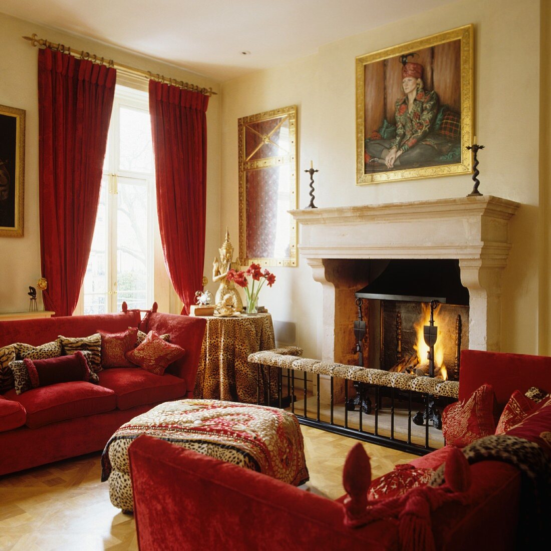 Two red Knole sofas and animal-skin print ottoman in front of classic fireplace