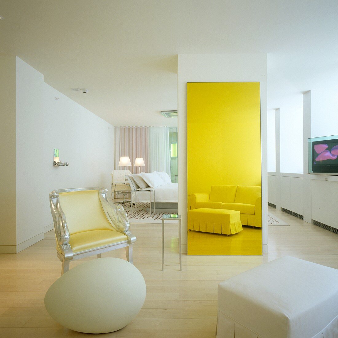 Weisses Hotelzimmer mit postmodernem Interieur - Sitzgruppe mit Sessel, Deko-Ei und klassischer Polstergarnitur als Reflektion im gelb getönten Spiegel