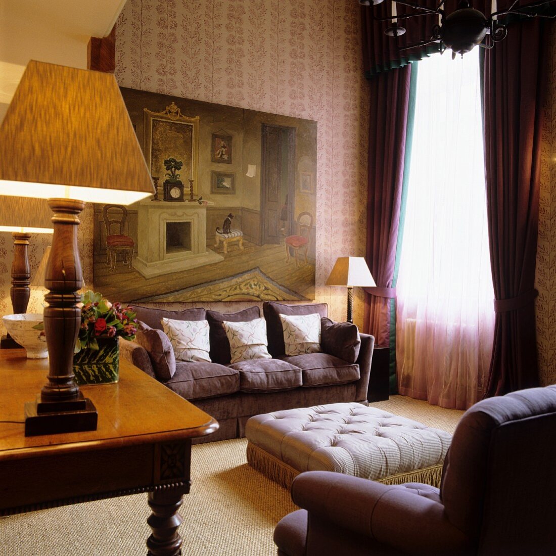 Grand salon with upholstered sofa and ottoman in front of window and table lamp on antique desk