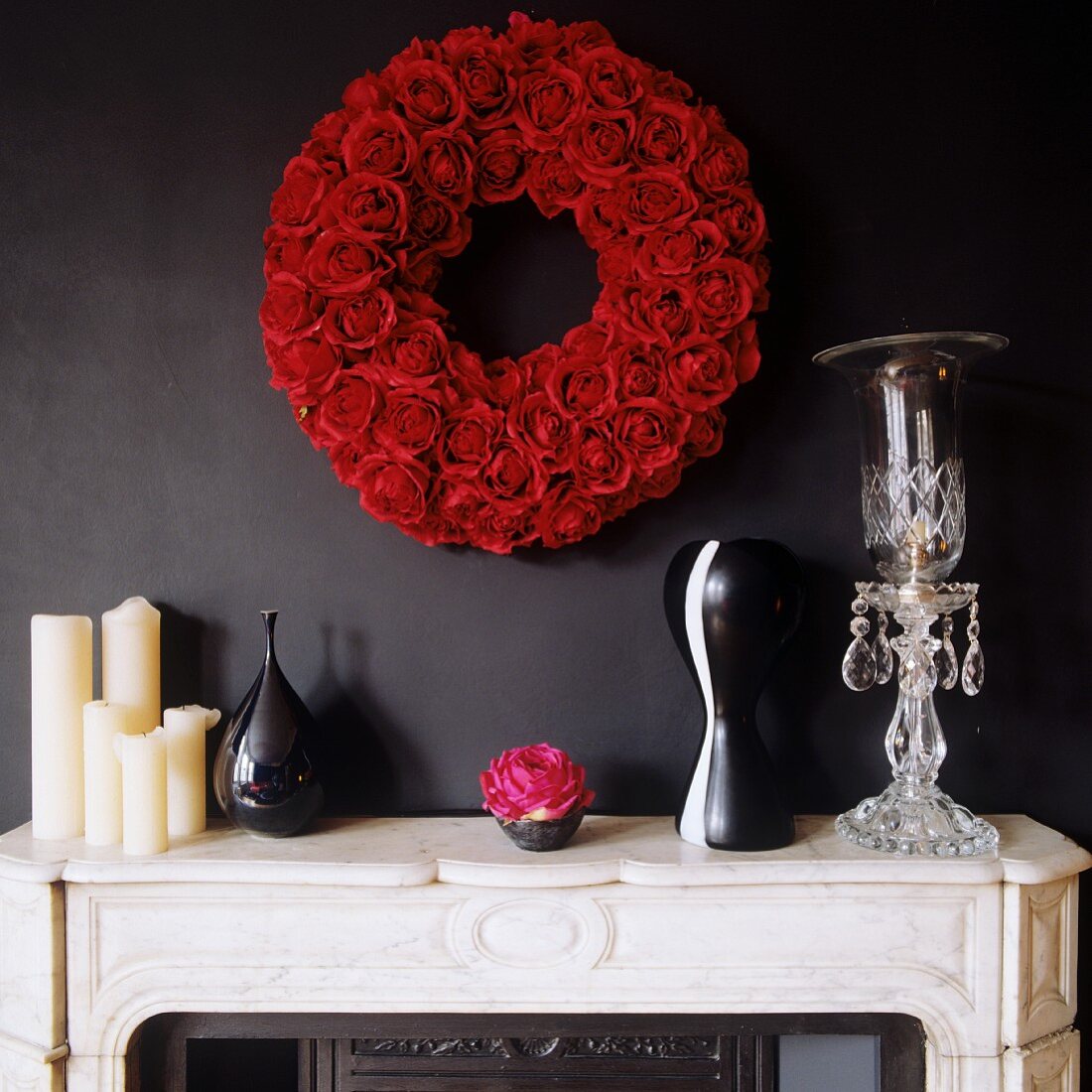 Kerzen und Vasen auf weißem Stein Kaminsims und Kranz aus roten Rosen an schwarzer Wand
