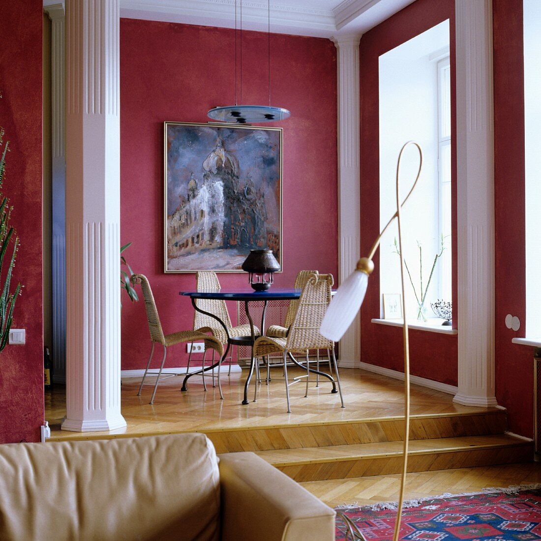 Traditionelles Wohnzimmer mit Tisch und Stühlen auf Empore und hellroter Bemalung neben weissen Stucksäulen an Wand
