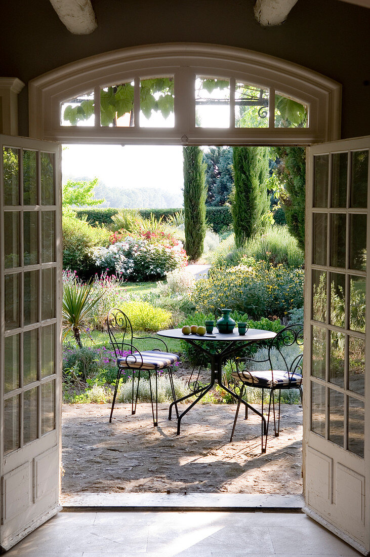 Blick durch die offene Terrassentür auf Tisch und Stühle in einem französischen Garten