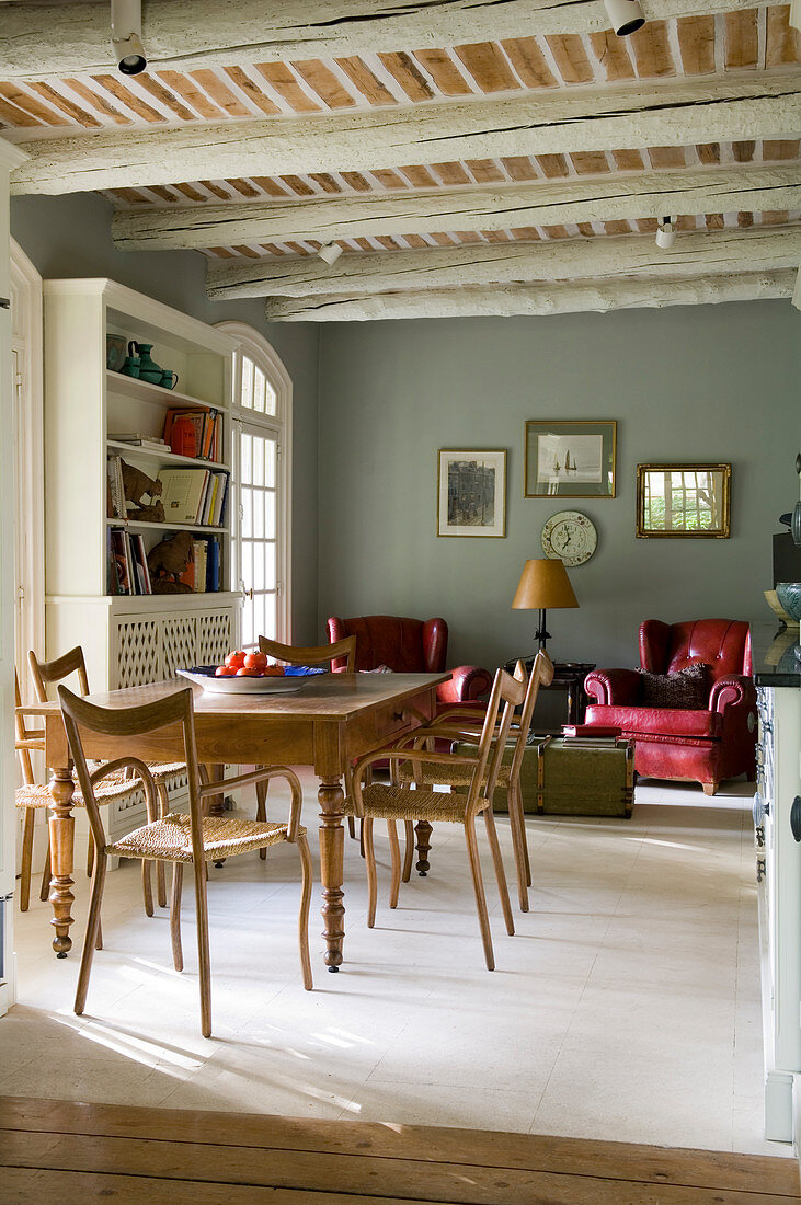 Antique dining table and wooden chairs in living-dining room of country house with rustic beamed ceiling