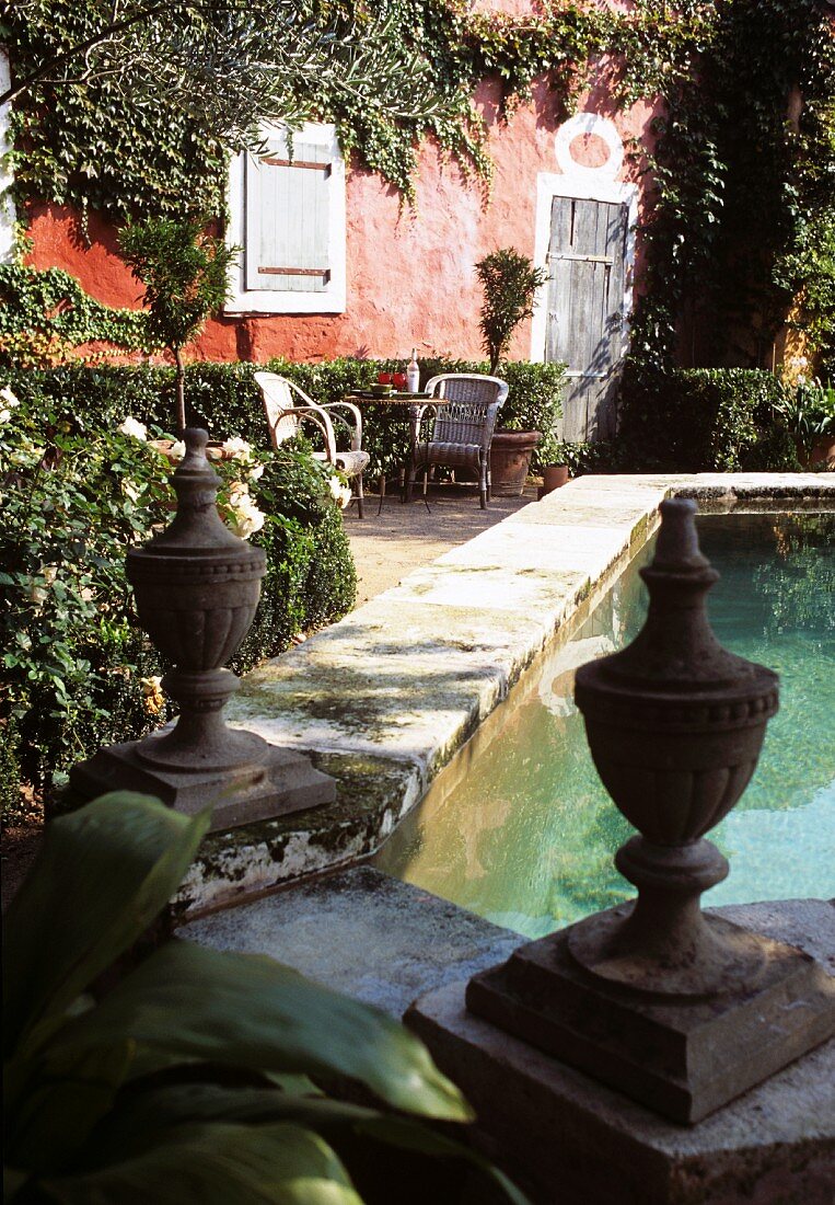 Lush, French garden with stone fountain and view of red house facade