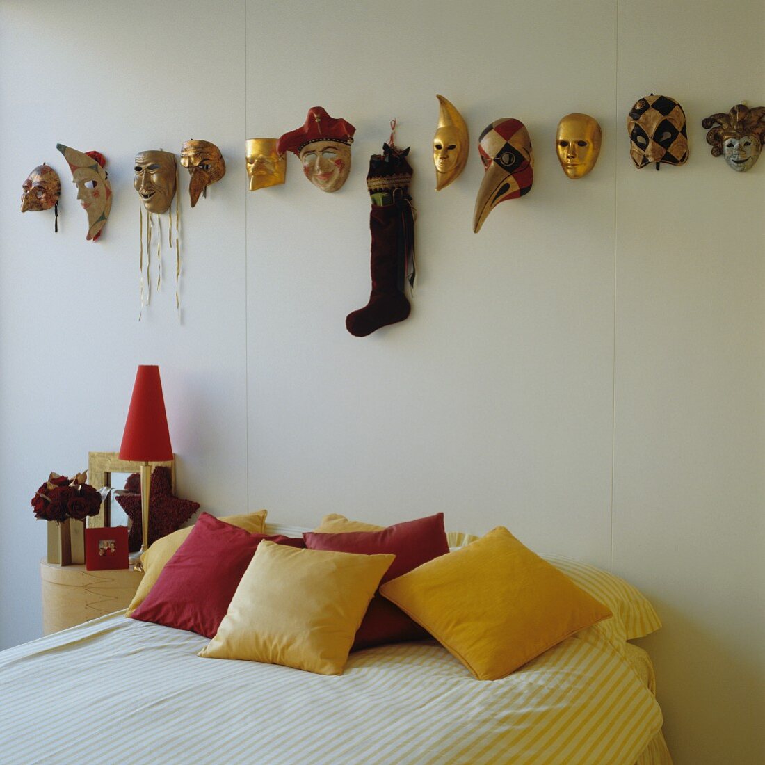 Bett mit gelben und roten Kissen unter venezianischen Karnevalsmasken