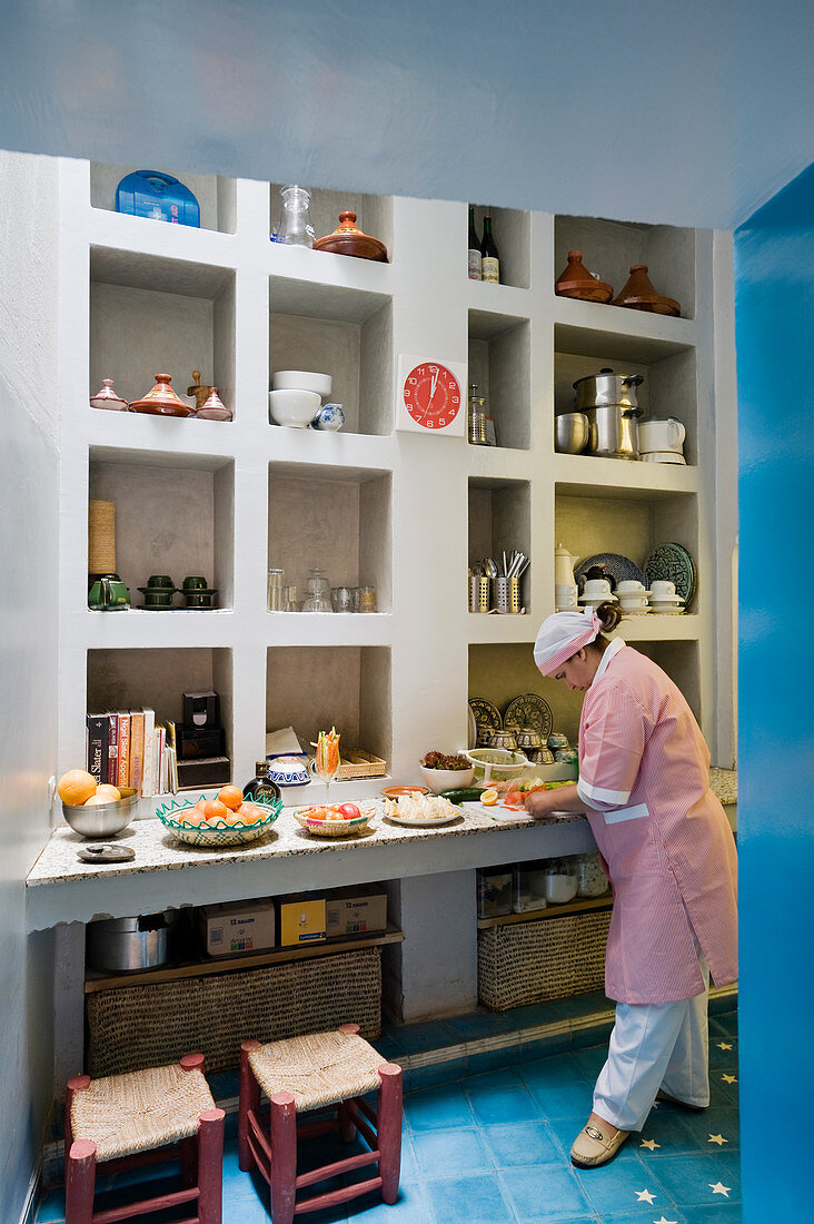 Blick durch Türöffnung auf Frau bei Zubereitung von Speisen auf Küchentheke vor gemauertem Wandregal