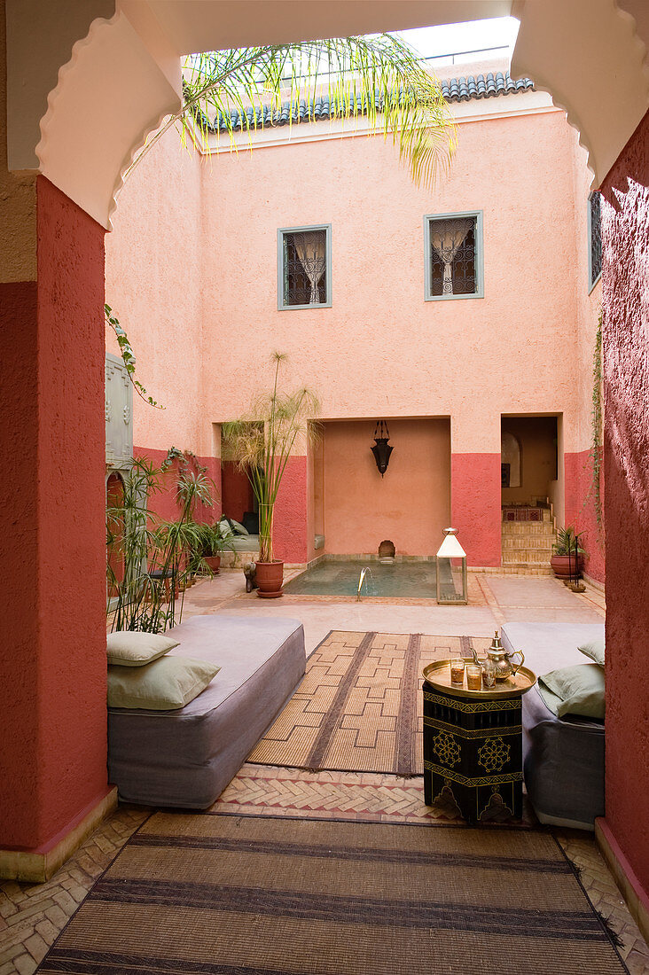 Blick durch hohes Tor in marokkanischen Innenhof auf Tagesbetten und Wasserbassin im Hintergrund