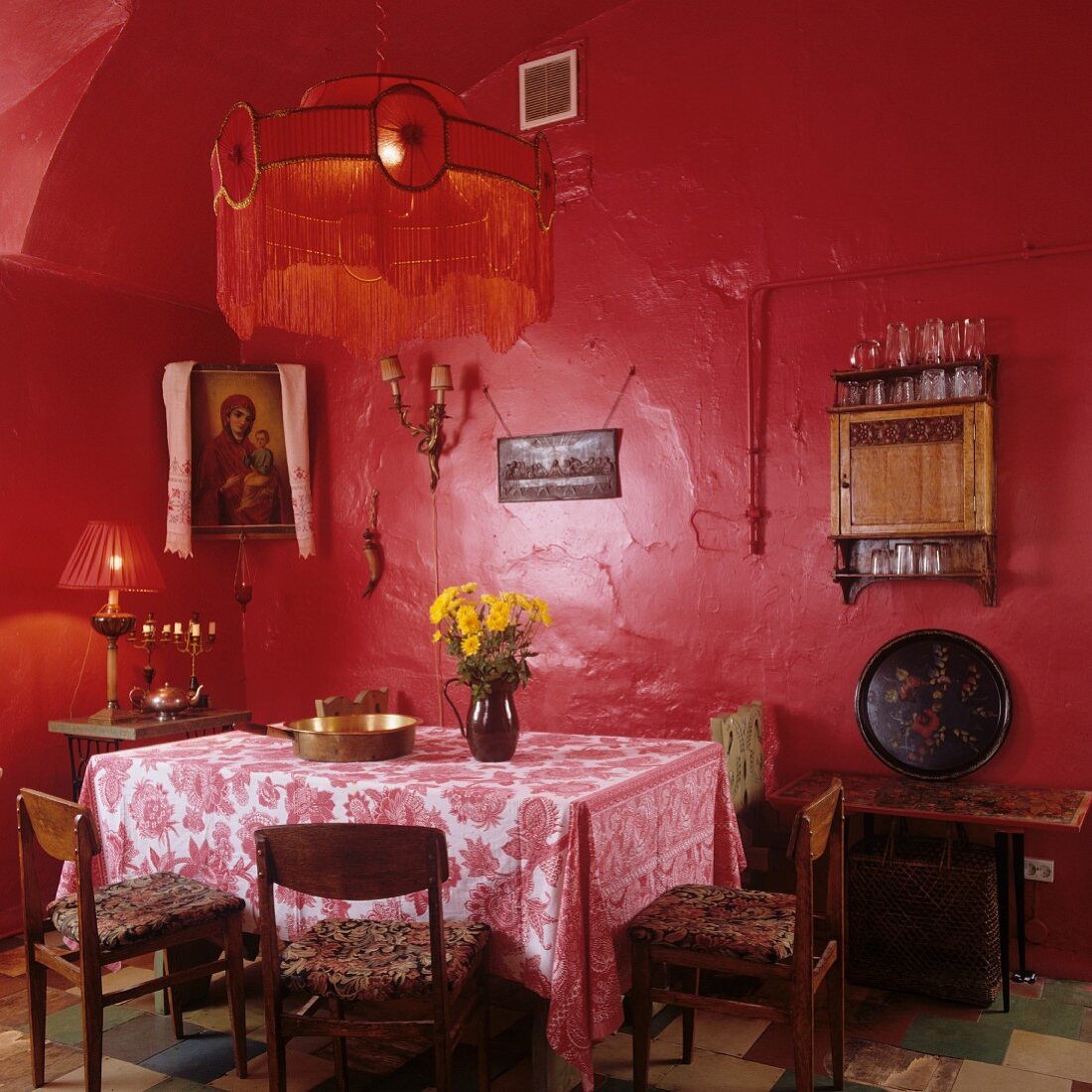 Simple dining room in red - table cloth on table below pendant lamp with fringed lampshade and red-painted walls