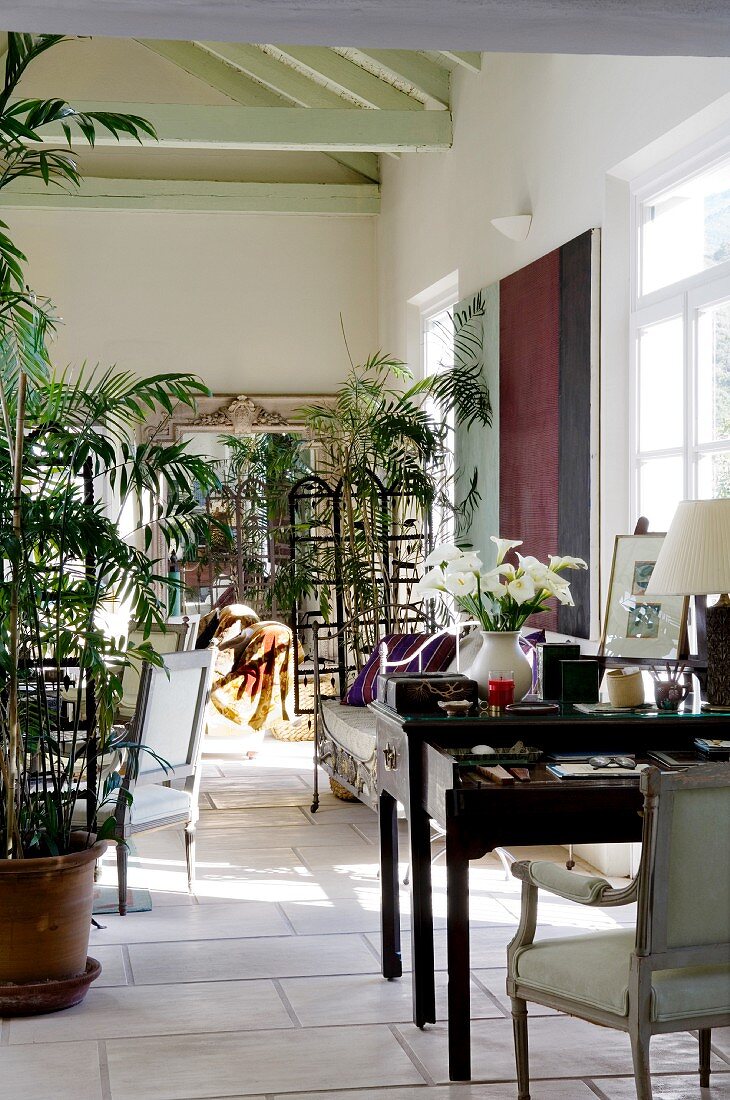 Mediterraner Wohnraum mit elegantem Arbeitstisch und Pflanzentöpfen vor transparenten Holzparavents