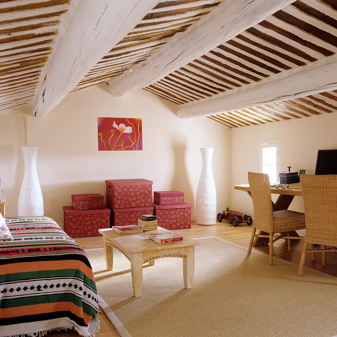Dachzimmer eines mediterranen Wohnhauses mit folkloristischer Tagesdecke auf Couch und gestapelten Aufbewahrungsschachteln vor Wand
