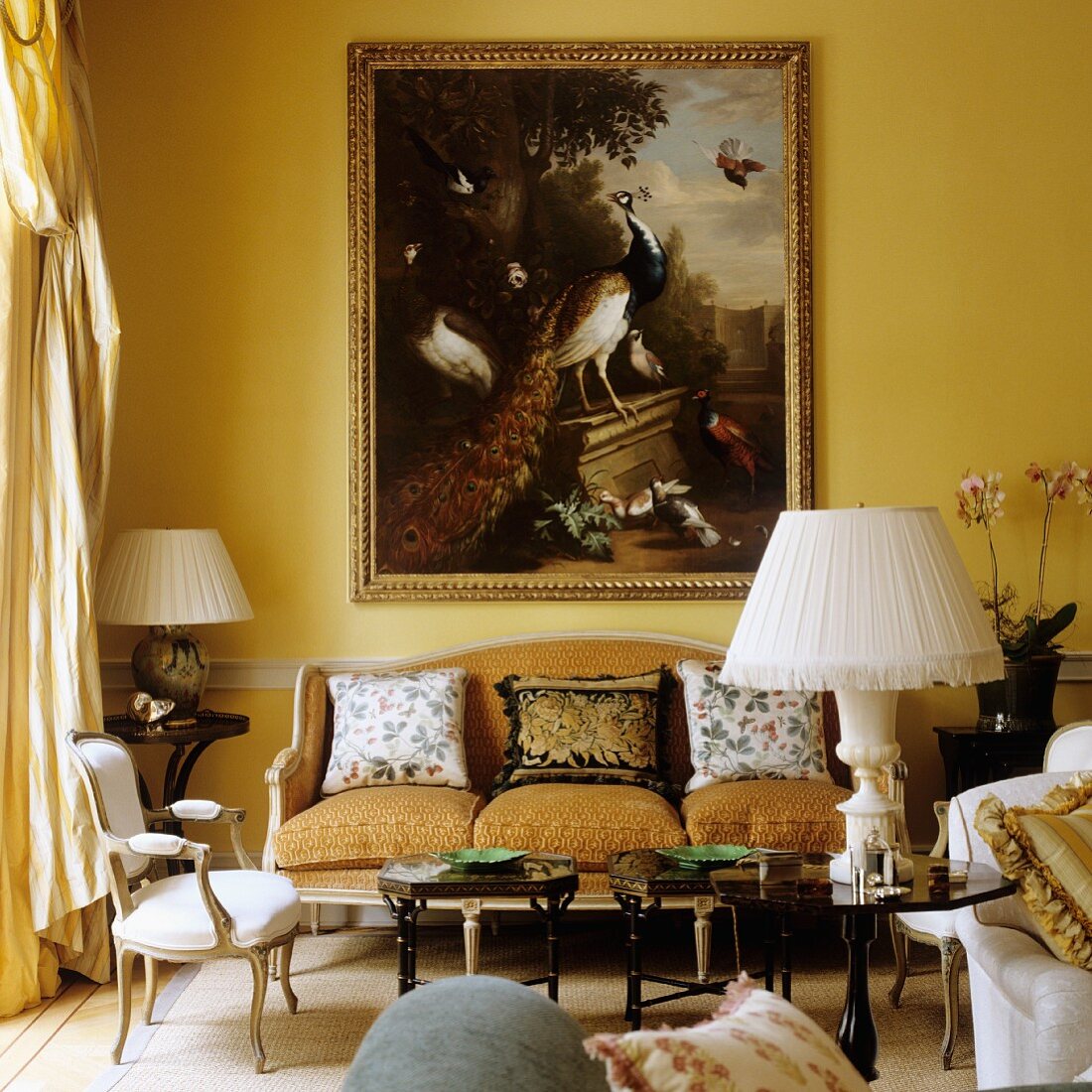 Tischlampe mit weißem Stoffschirm auf kleinen Beistelltisch vor Sitzbank im Rokokostil und altes Gemälde an gelb getönter Wand
