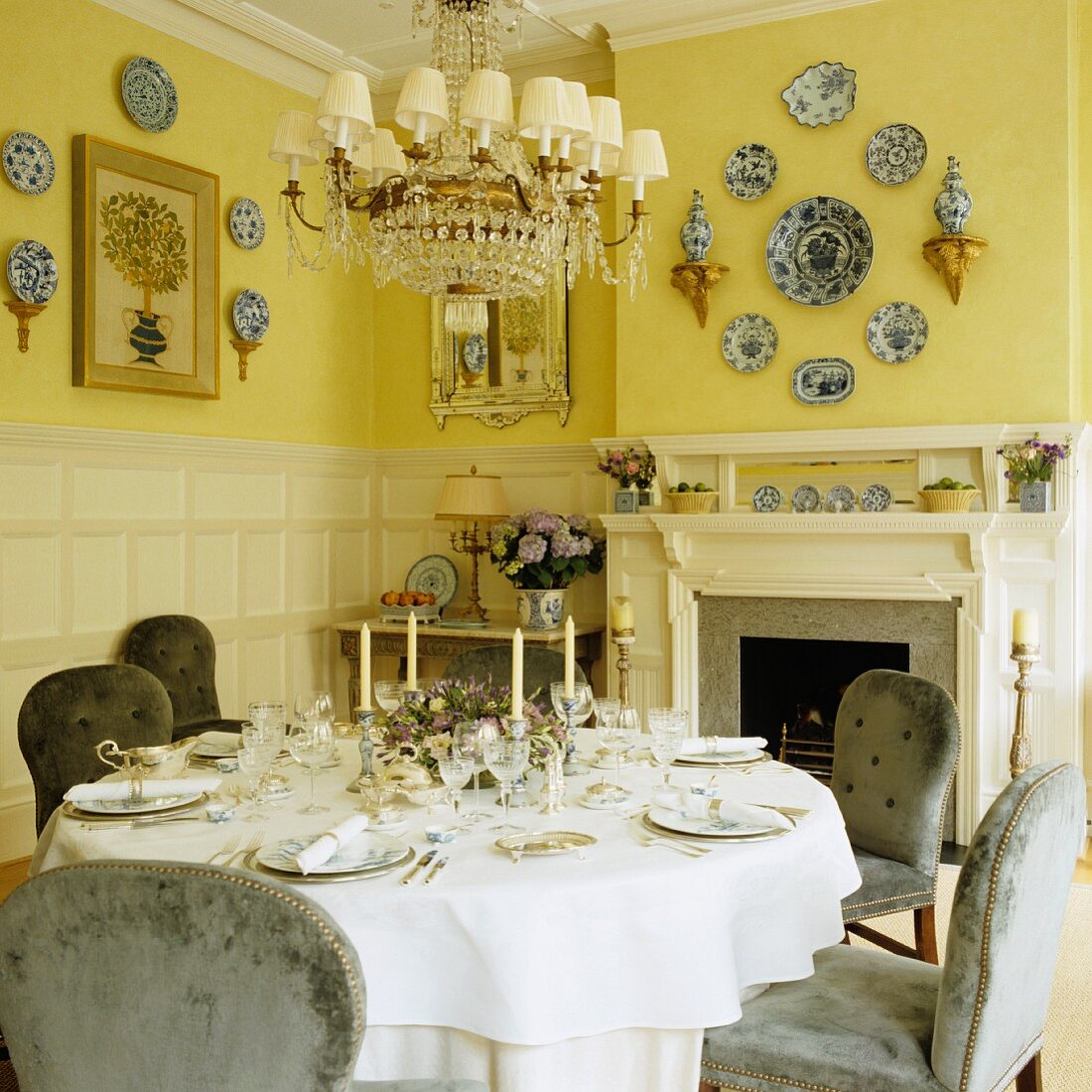 Festlich gedeckter Tisch vor offenem Kamin und an gelb getönten Wänden befestigte Deko-Teller