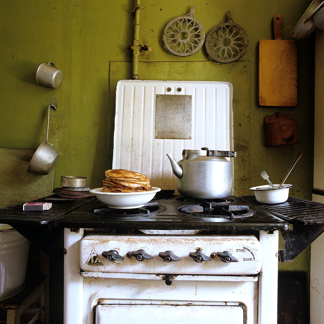 50er Jahre Herd in schlichter Küche, mit einem Teller frisch gebackener Pfannkuchen und einem Wasserkessel