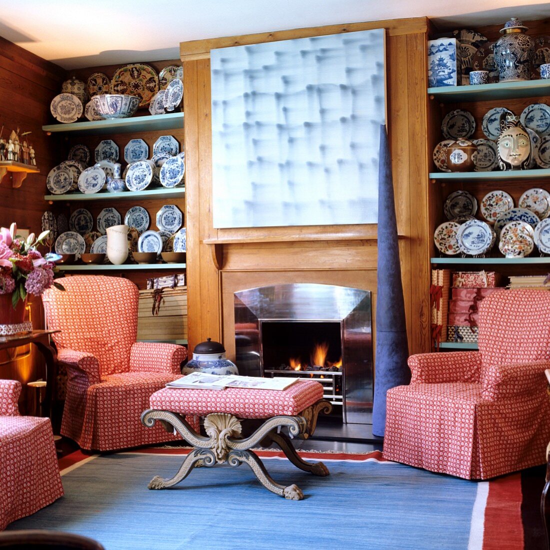 Traditionelle Wohnzimmerecke - Sessel mit karierter Husse und passendem Couchtisch vor Kamin zwischen Regalen mit bemalten Wandtellern