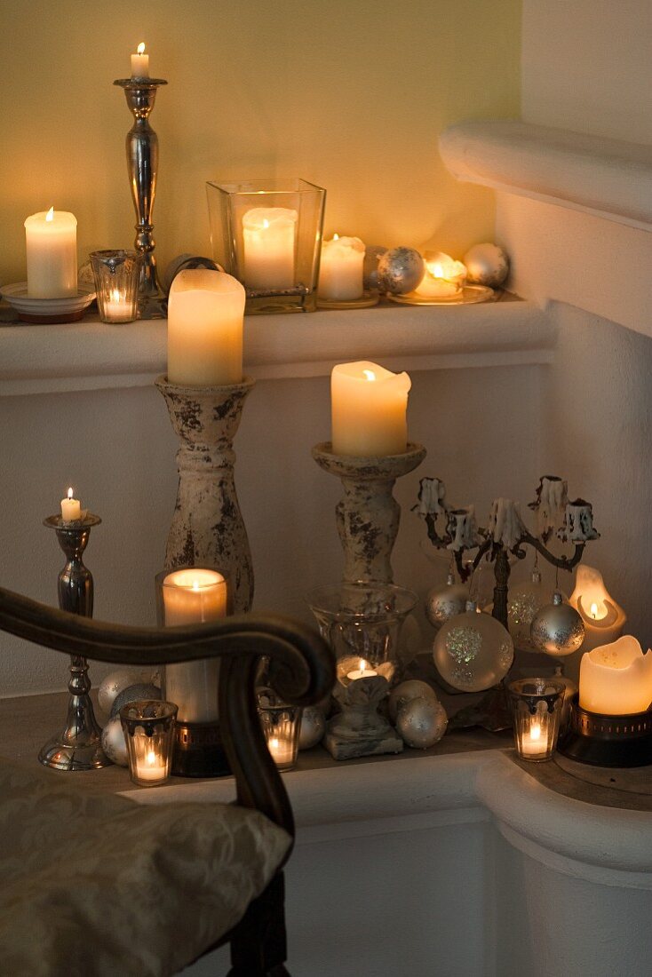 Various lit candles on candle sticks and holders in corner