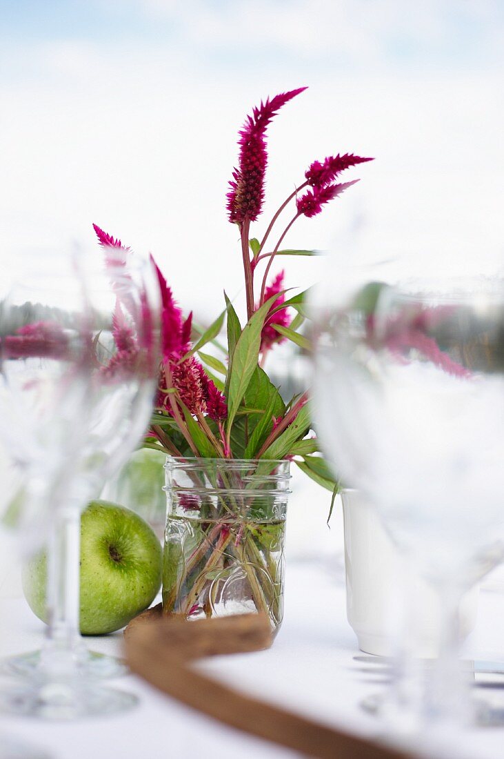 Wildblumen, Apfel und Weingläser auf gedecktem Tisch