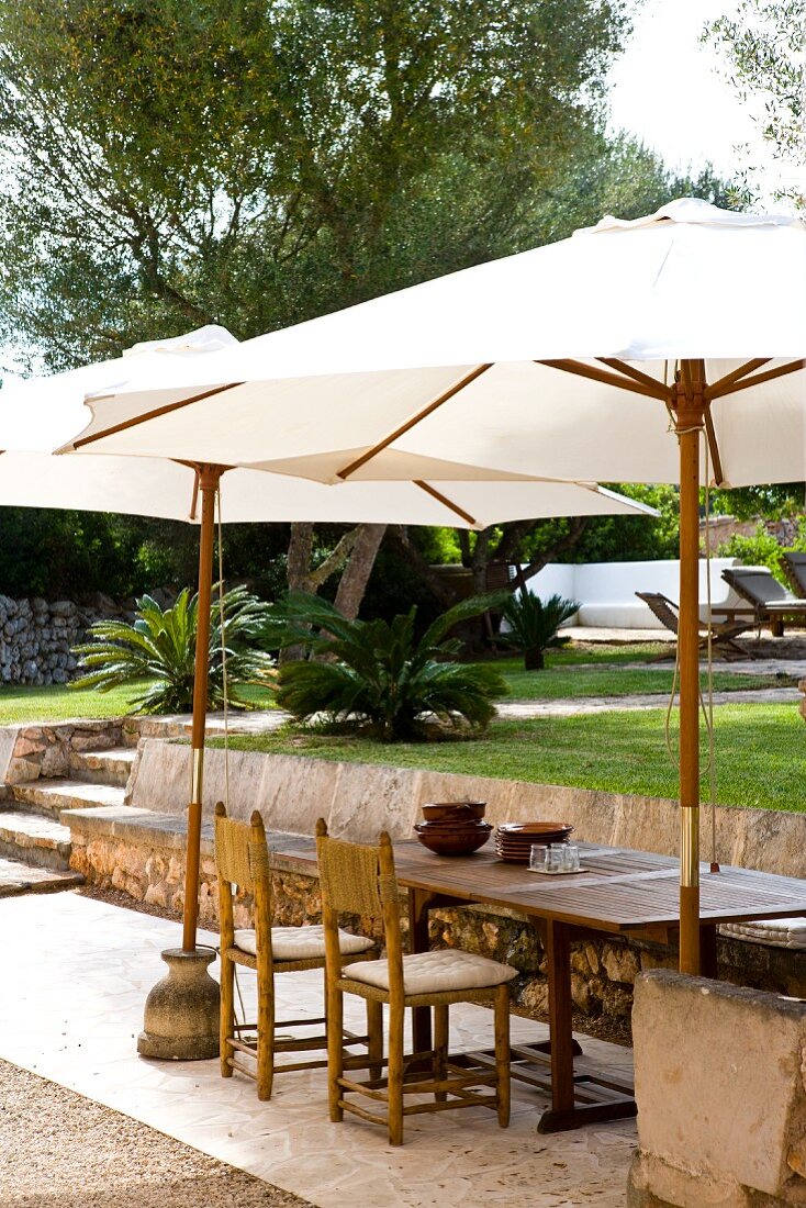 White parasols shading seating on terrace in Mediterranean garden