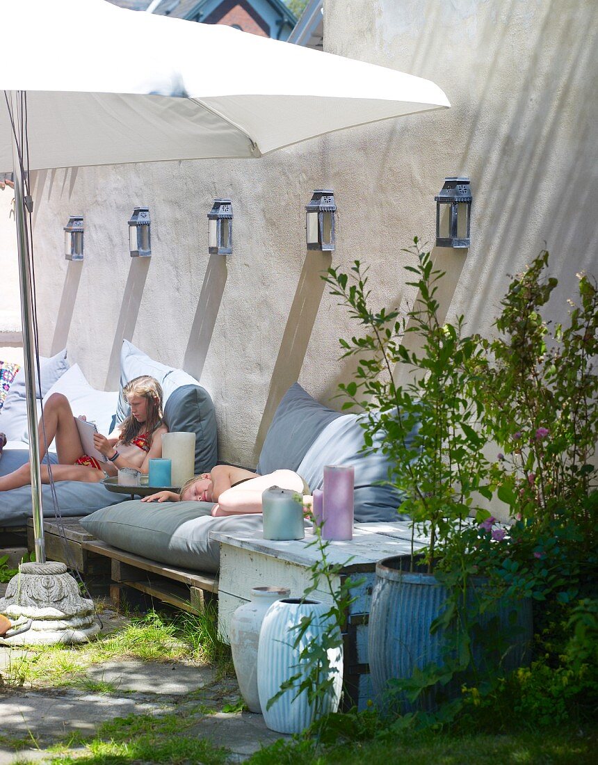 Kinder chillen auf Gartenmöbel mit Polstern unter Sonnenschirm