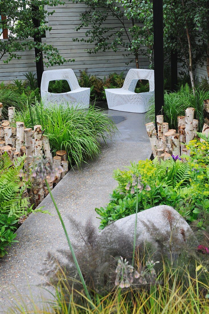 Üppig begrünter Gartenweg und Sitzecke mit zwei Gartenstühlen