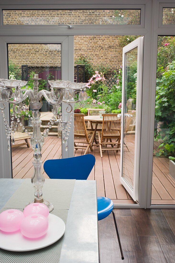 Blick von der Wohnküche durch die geöffnete Terrassentür auf einen begrünten Patio mit Holzplankenboden