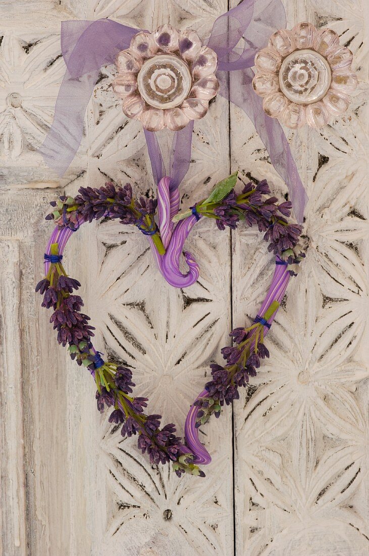 Dekokranz in Herzform mit Lavendelblüten am Türknauf eines weissen Kleiderschranks mit floralen Schnitzereien