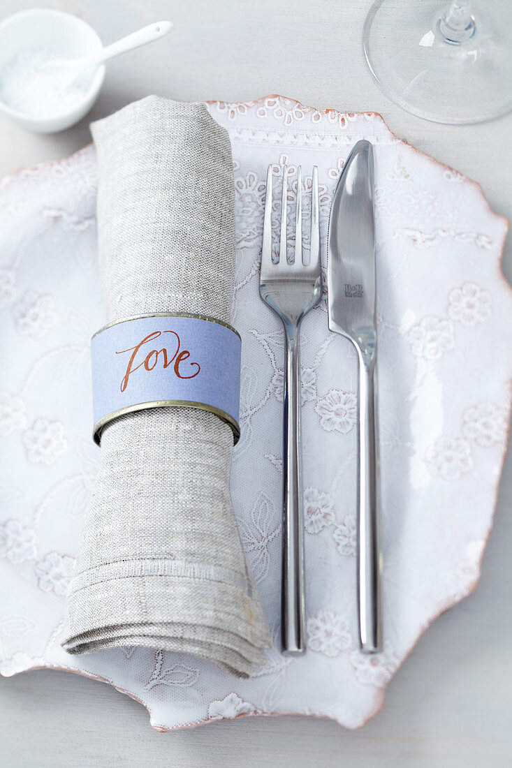 A place setting with cutlery and a homemade napkin ring made from a small tin can
