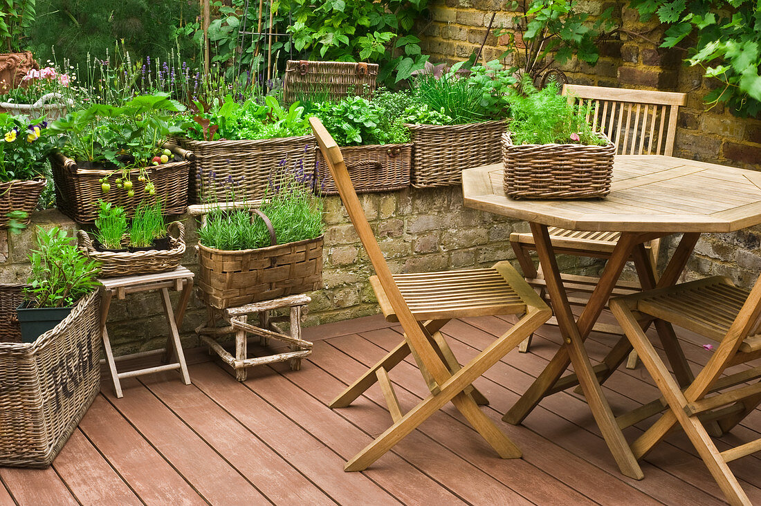 Tisch mit Stühlen und Pflanzkörbe mit Kräutern und Salat auf einer Terrasse