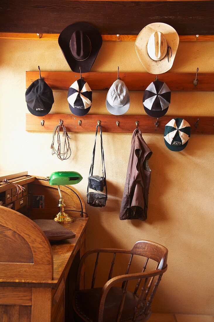Garderobe mit hängenden Hüten und Kappen über Schreibtisch und Stuhl aus Holz im Vintagestil