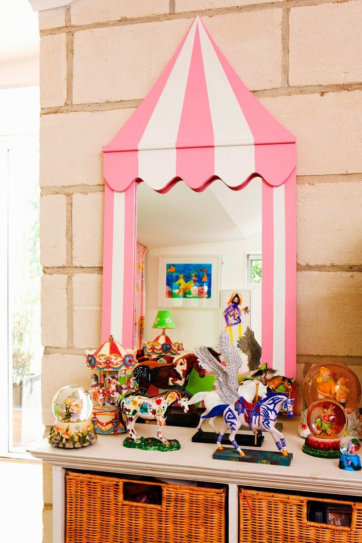 Toys on cabinet in front of mirror with whimsical frame leant on a stone wall